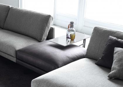 Detalle del elegante puf de piel y del plano de apoyo en combinación con el sofá de tela Dee Dee - BertO